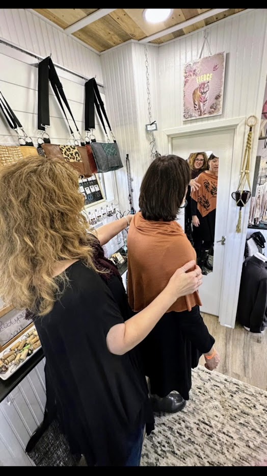 Two ladies shopping in a clothing store- one lady trying on a poncho