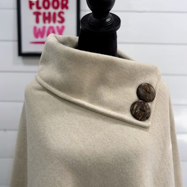 Cream poncho coat with brown buttons on a black mannequin form.