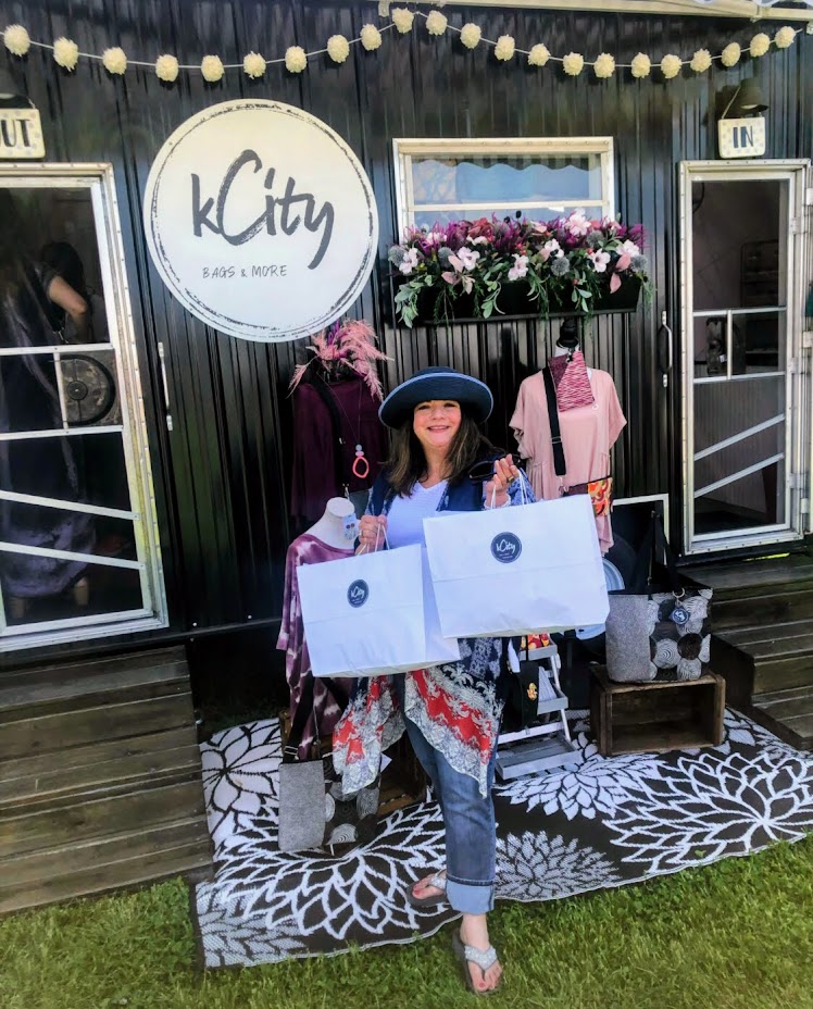 Lady with brown hair and hat holding shopping bags in front of a black trailer.