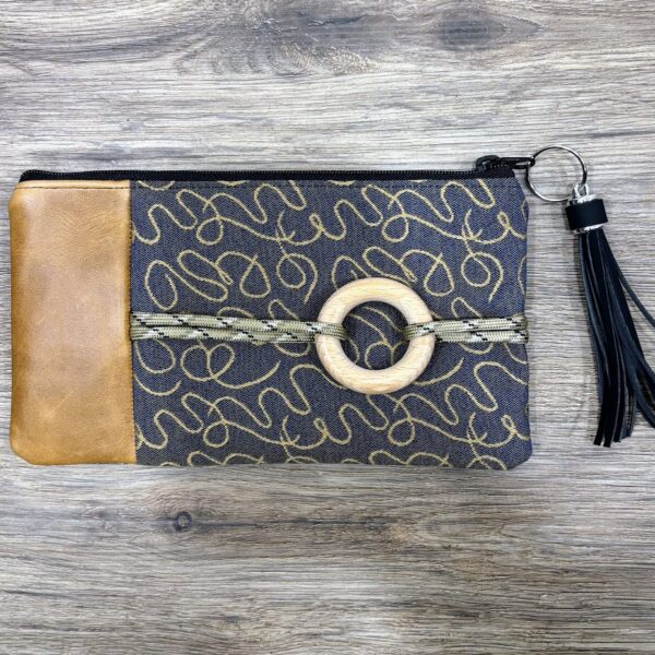 Custom bag-dark denim blue fabric with caramel color squiggle design-caramel leather-rope across front with wooden circle-black tassel-wood grain backdrop.