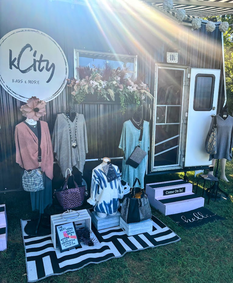 black trailer, business sign on front-kcity bags & more, clothing displays with custom bags and jewelry, window box with flowers.