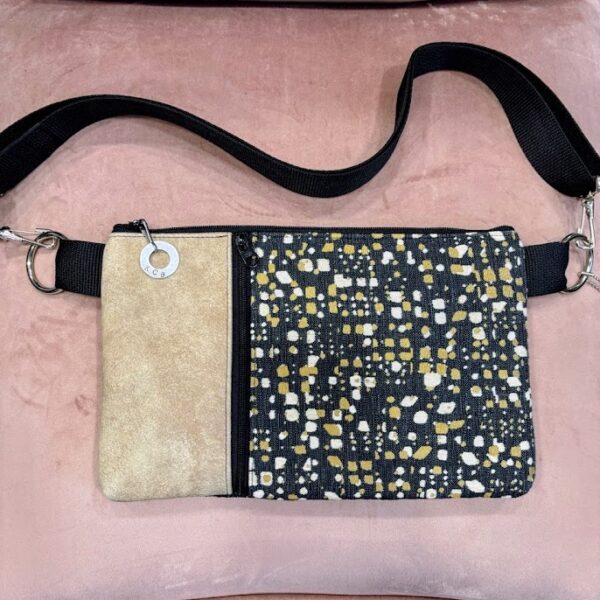 Custom crossbody bag with navy fabric printed with tan and cream design-front black vertical zipper with tan leather strip. Pink background.