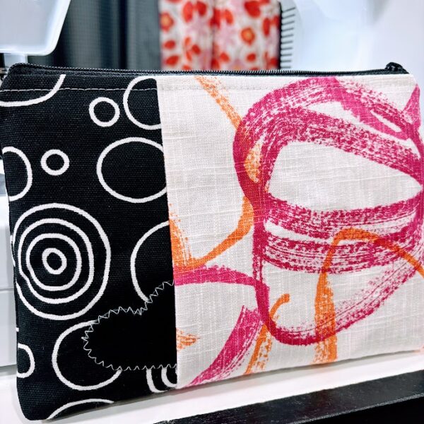 Custom cosmetic bag-black, white, pink, orange print-black leather heart with white stitching-sewing machine and curtain background.