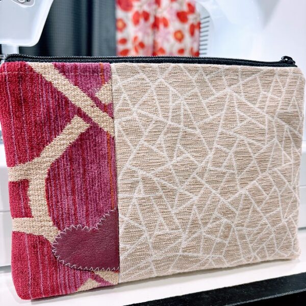 Custom cosmetic bag with tan, white, pink print fabric-leather heart white stitching-sewing machine print curtains in background.