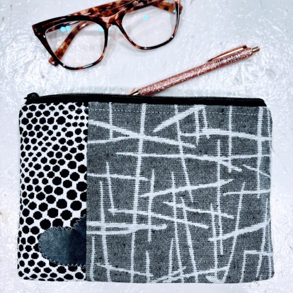 Custom cosmetic bag with grey, black, white print fabric-black leather heart with white stitching-white background. Brown eyeglasses and sparkle pen. white background.